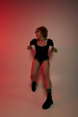 A young curvy redhead woman in a bodysuit dancing energetically in front of a striking red background. clipart