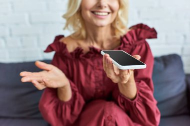 Şık giyinmiş olgun bir kadın koltukta oturuyor, cep telefonuna dalmış..