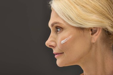 Olgun bir kadın ışıldayan yüzüne krem sürer..