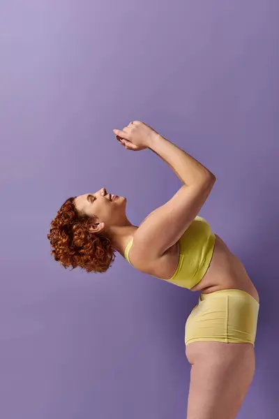 stock image Curvy redhead woman in yellow bikini posing gracefully against a vibrant purple wall.