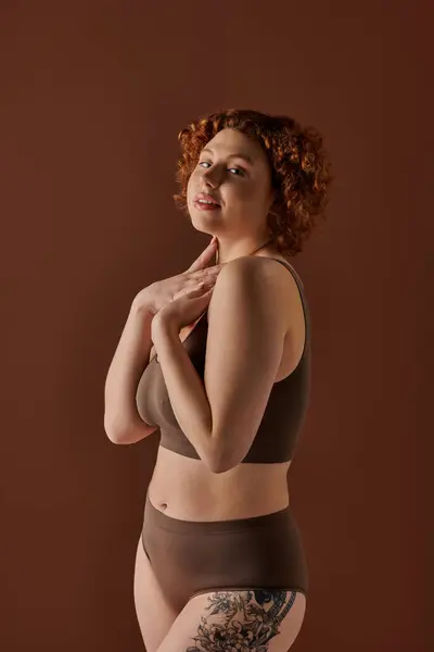 stock image A young, curvy redhead woman confidently poses in a brown bikini.