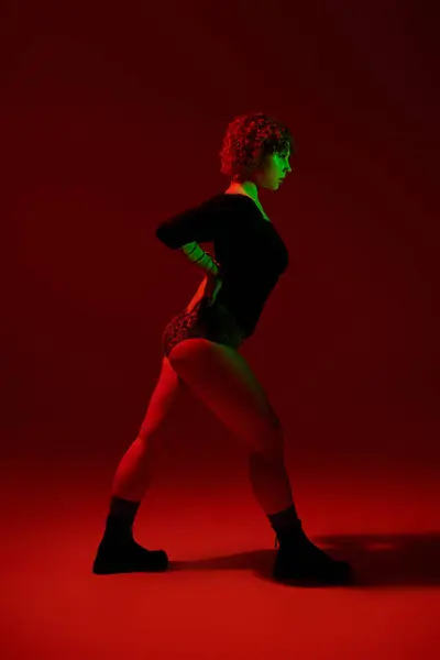 stock image A young, curvy redhead woman stands confidently in front of a vibrant red background.