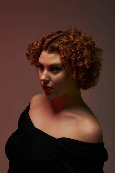 A young curvy redhead woman in a bodysuit poses confidently on dark background.