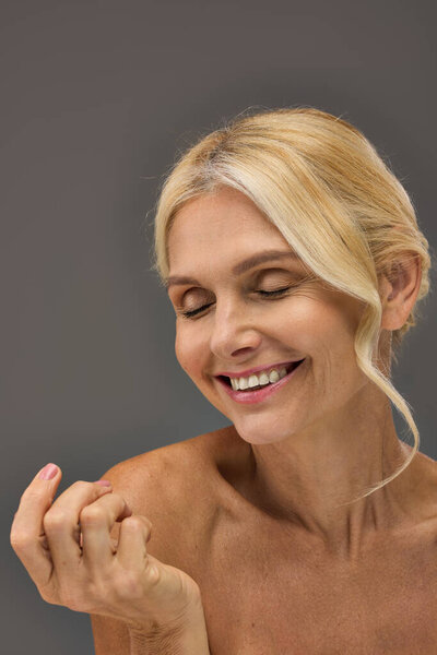 A mature woman gracefully smiles with closed eyes.