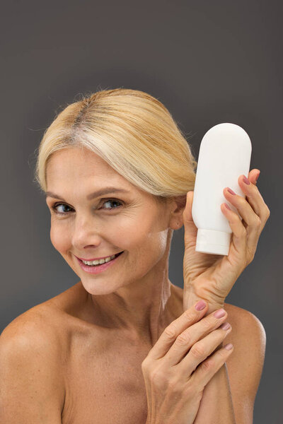 Beautiful mature woman holding locion on a gray backdrop.