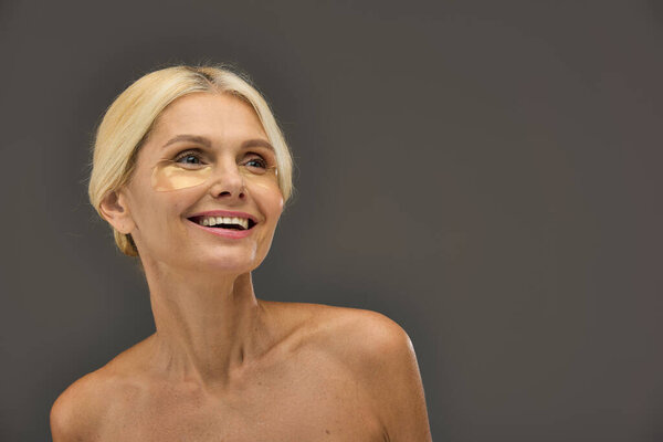 Appealing mature woman with blonde hair with eye patches on a gray backdrop.