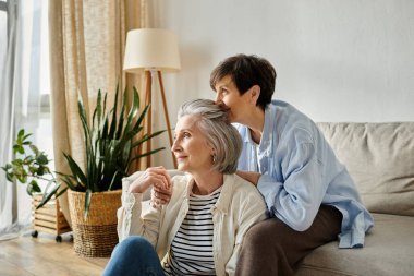 Two elderly women enjoy each others company on a comfortable couch in a warm living room. clipart