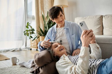 Two women laying on floor, capturing a selfie. clipart