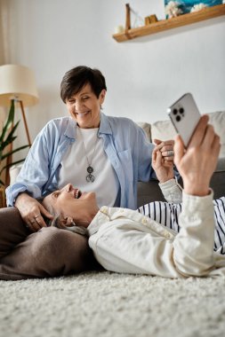 Two senior women laying on the floor, capturing a selfie moment of joy and friendship. clipart