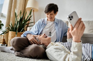 One woman lays on the floor while the other looks at her phone. clipart