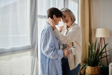 Two elderly women share a heartwarming hug in front of a window. clipart