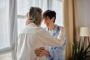 Two elderly women share a heartwarming hug in front of a luminous window. clipart