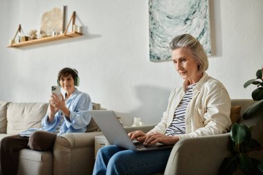 İki kadın kanepede dizüstü bilgisayarla meşgul olmanın keyfini çıkarıyor..