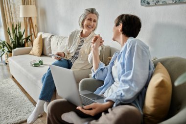 İki insan, sevecen bir lezbiyen çift, bir kanepede oturup dizüstü bilgisayarla konuşuyorlar..