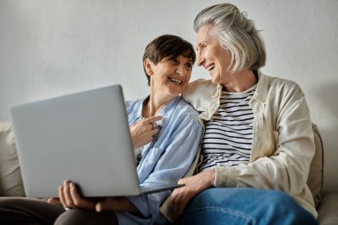 Two older women sitting on a couch, engaged with a laptop. clipart