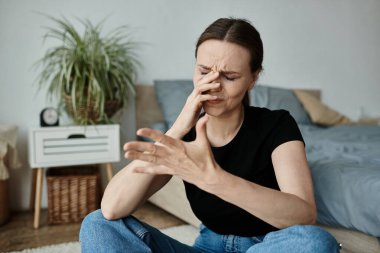 Middle-aged woman sits on floor, hand on nose, lost in thought.