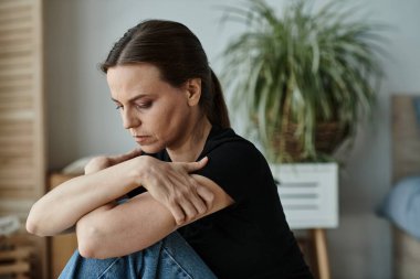 Middle-aged woman sitting on floor, hands on knees in deep thought.