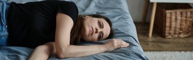 A middle-aged woman lies on a bed with crossed arms.