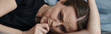 Middle-aged woman laying on bed with hand on head, deep in thought.