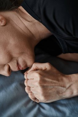 Middle-aged woman lays on a bed, hand on face, deep in thought.