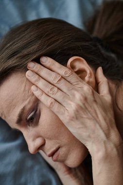 Middle-aged woman lies in bed, hands on head, deep in thought.