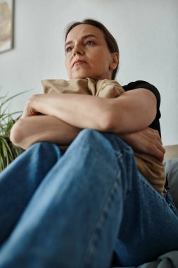 Middle-aged woman sits on couch with arms crossed.