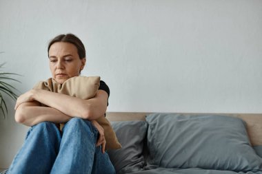 A middle-aged woman sits on a bed, arms crossed, showing resilience.