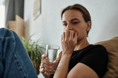 Woman finds solace, holding water on couch.
