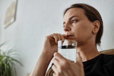 A woman finds solace on her couch, holding a glass of water.