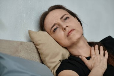 Middle-aged woman lying in bed with hand on chest.