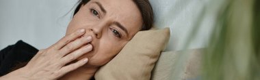 A middle-aged woman laying down with her hand on her face, deep in thought.