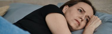 Middle-aged woman laying down, pondering with hand on head.