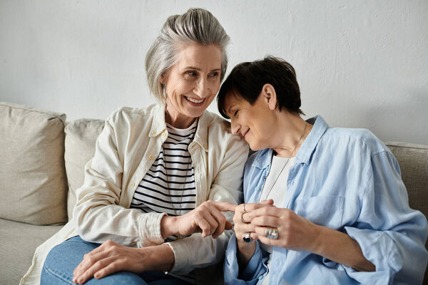 Two women, a loving mature lesbian couple, sit closely on a couch, engrossed in conversation.
