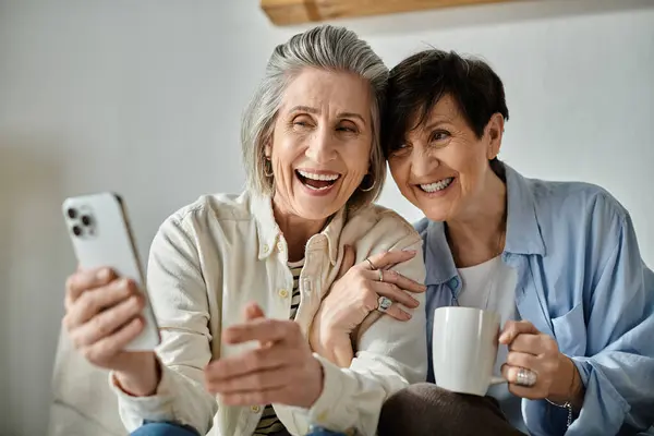 stock image Two elderly women sit on a couch, enjoying a cup of coffee together.