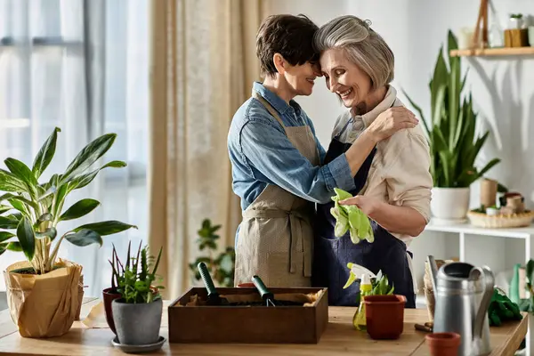 Stock image Two older women share a heartfelt hug in a cozy kitchen surrounded by green plants.