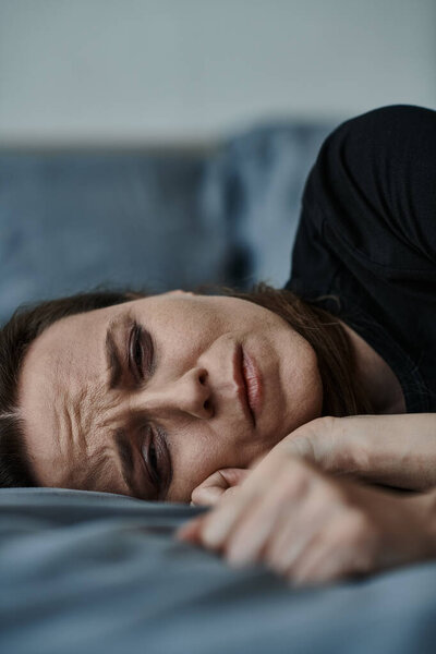 A woman lays on bed, hand on face.