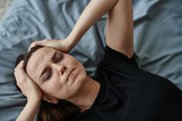 Middle-aged woman lying in bed, hands resting on head, contemplating.