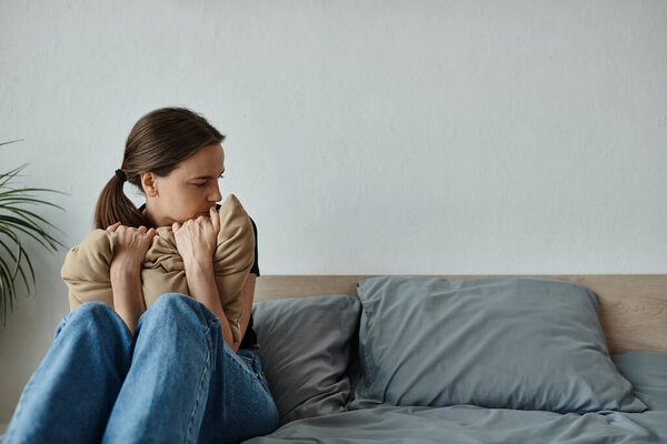 A middle-aged woman sits on a couch, holding a pillow under her arm.