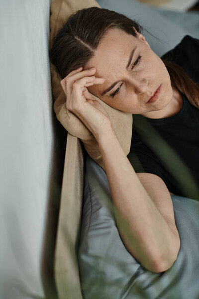 Middle-aged woman lying in bed, head on pillow, lost in thought.