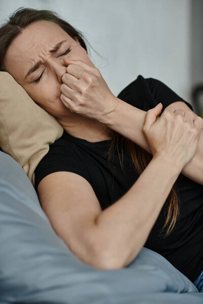 A middle-aged woman laying on a bed with her hand covering her face in a moment of reflection.
