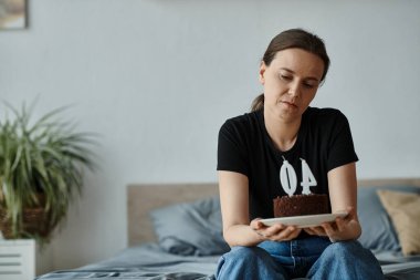 Middle-aged woman seated with chocolate cake on bed.