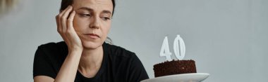 A woman joyfully holding a cake with a 40 candle on it.