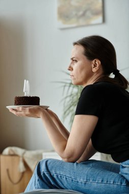 Woman sitting on couch, holding birthday cake.