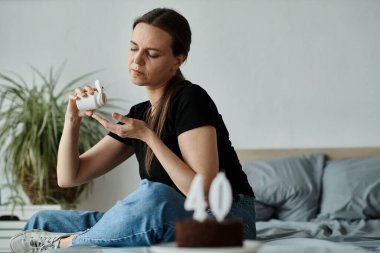 Woman seated on bed, deep in thought with her coffee cup.