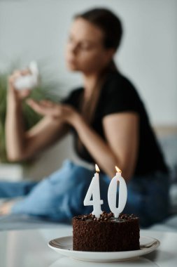 Woman sitting beside a 40th birthday cake on a bed. clipart