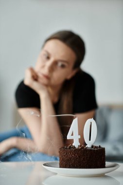 Middle-aged woman gazes at a birthday cake, pondering the significance of turning 40. clipart