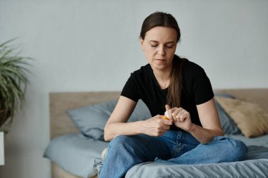 Middle-aged woman sitting on bed with hands on knees in thoughtful contemplation.