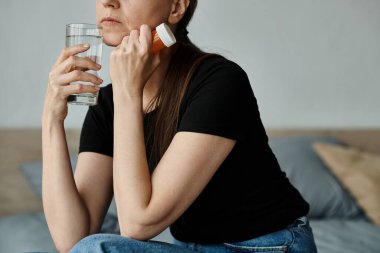 Middle aged woman with glass of water sitting on bed.