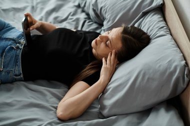A woman in bed, holding her phone.