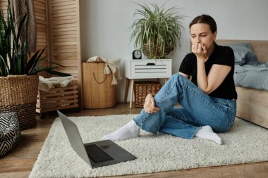 Middle aged woman sitting on floor in front of laptop, immersed in contemplation.